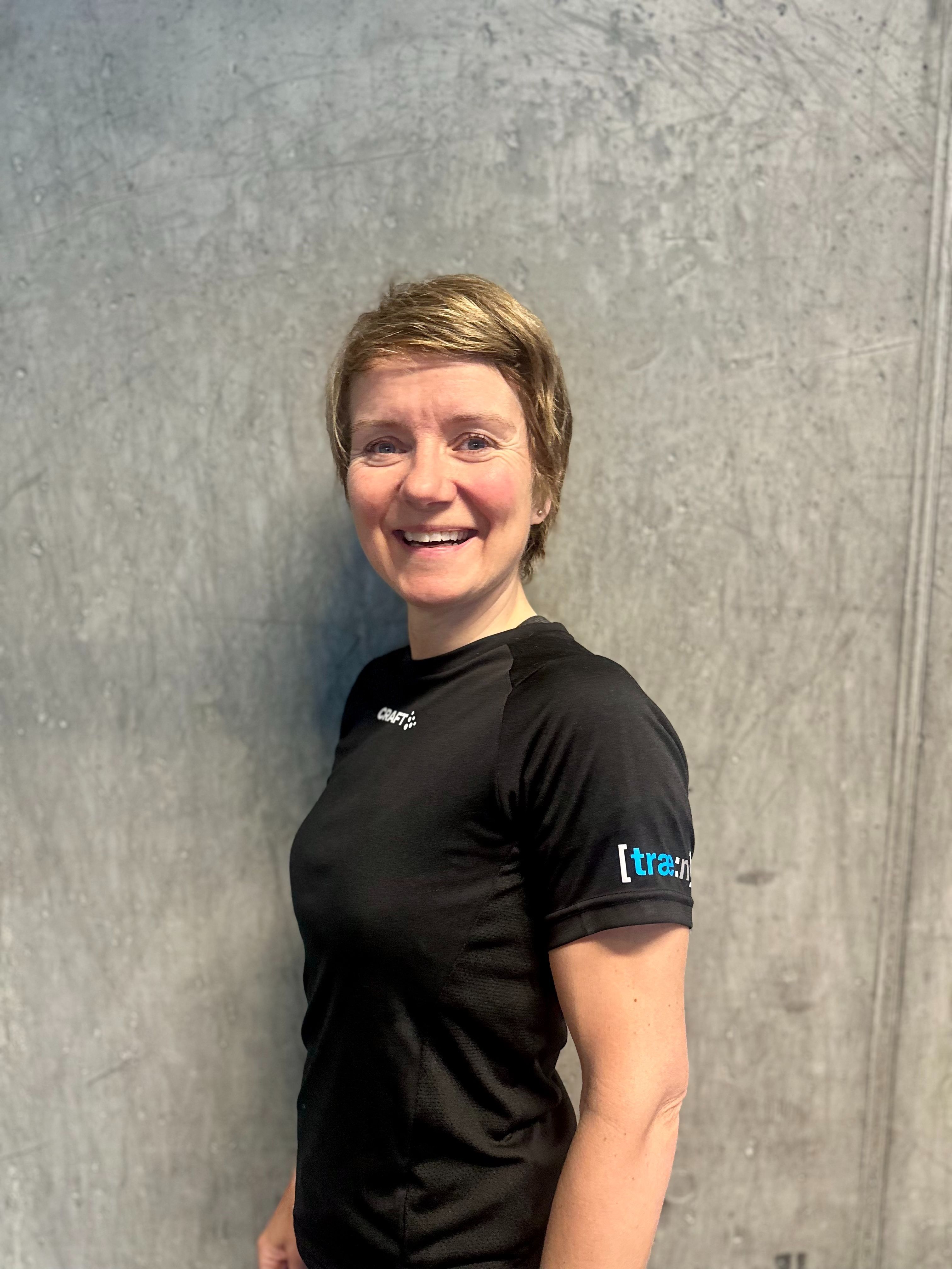 Kvinne sitter på gulvet ved kettlebell og vannflaske i treningsstudio.